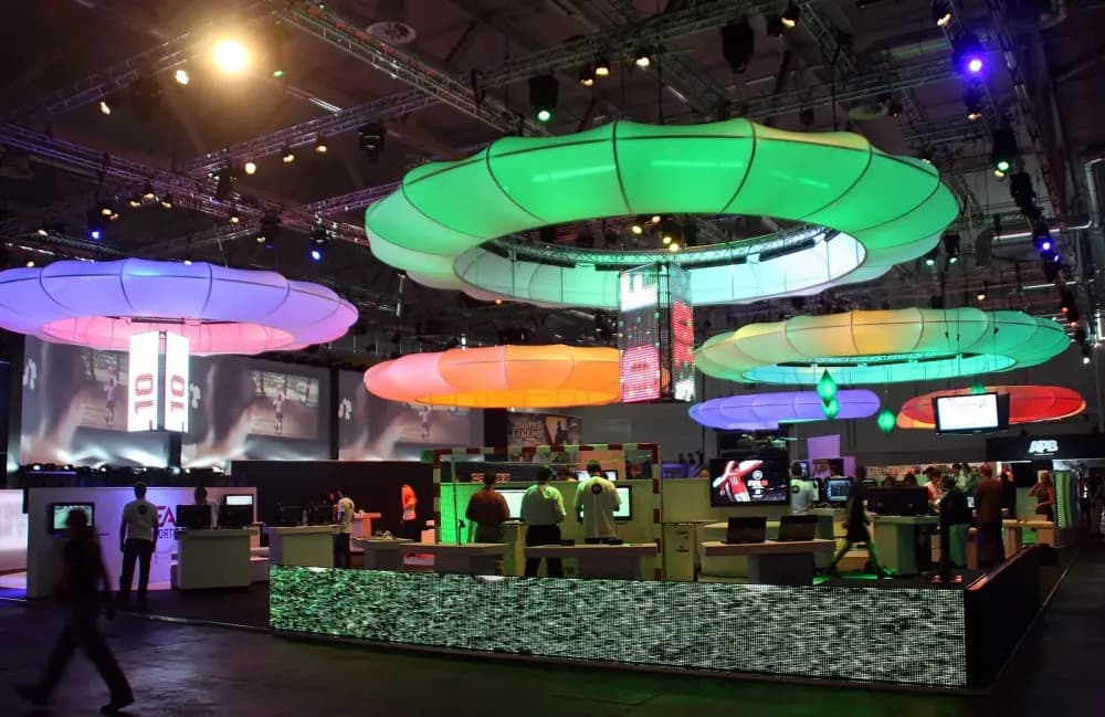 Convention hall interior with glowing overhead circular installations and exhibition booths.